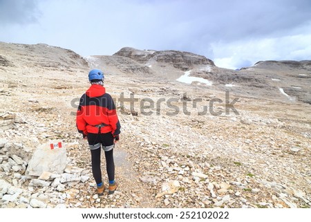 Isolated woman climber crossing Meisules plateau on rocky trail, Sella massif, Dolomite Alps, Italy