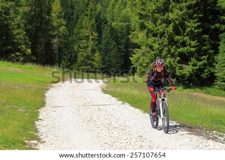 Woman cyclist pedaling on sunny road on the way to Sella pass, Dolomites Alps, Italy