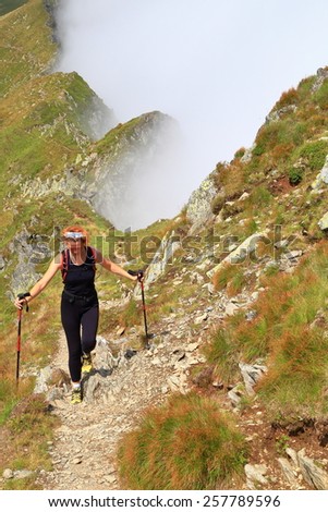 Woman hiker walking on alpine trail above the clouds