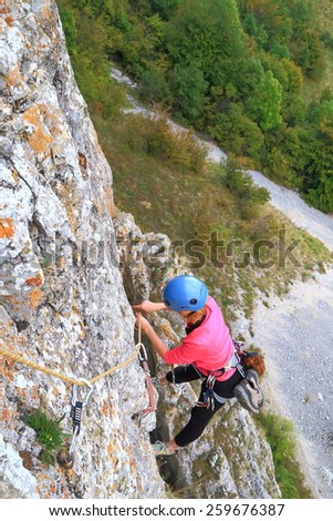 Woman removes protection gear while hanging on the rope high above ground