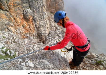 Woman climber clipping protection gear to the steel cable along via ferrata \