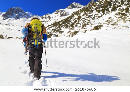 Mountaineer carries heavy backpack and climbing gear in sunny winter day