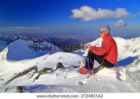Woman mountaineer seated on snow covered mountain in sunny winter day