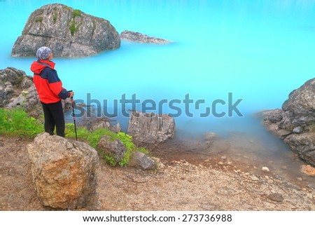 Large boulders on the shore of Sorapis lake with hiker woman standing in the rain, Dolomite Alps, Italy