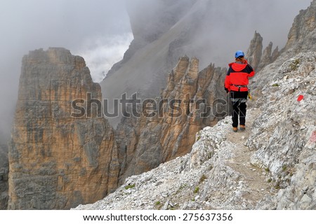 Remote climber on a trail above tall cliffs surrounded by clouds, Tofana massif, Dolomite Alps, Italy