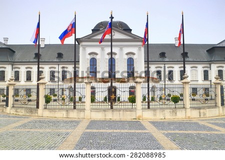 White building of the Presidential Palace (Grassalkovich Palace) with tall flags waving under overcast sky, Bratislava, Slovakia