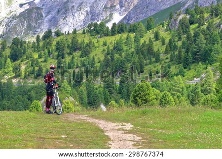 Woman cyclist standing near mountain bike in the area of Sella pass, Dolomites Alps, Italy