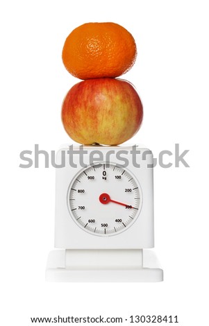 Tangerine and apple on kitchen scales. Vertical format over a white background