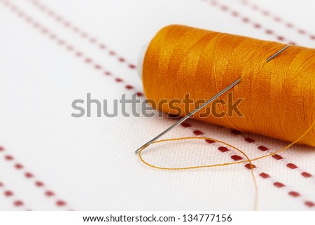 Bobbin of orange thread with needle on fabric. Sew accessories on blurred background.