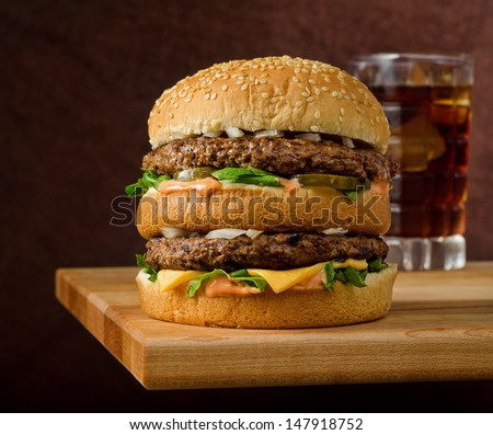 A classic style double cheeseburger with two beef patties sauce lettuce cheese pickles and onions on a sesame seed bun with soda A classic style double cheeseburger with two beef patties sauce lettuce cheese pickles and onions on a sesame seed bun with soda