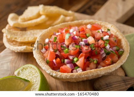 Fresh tomato salsa with serrano pepper, red onion, green onion, lime, and cilantro in a tortilla bowl.