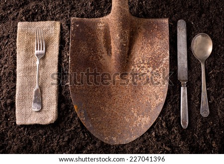 Rusty shovel organic farm to table healthy eating concept on soil background with fork, knife, spoon, and napkin.