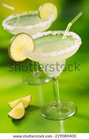 Two tequila margaritas with tequila, lime, and salt against a vibrant abstract green background.