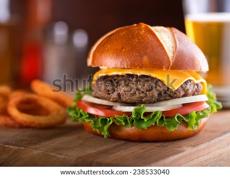 A delicious gourmet cheeseburger on a pretzel bun with lettuce, onion, and tomato.
