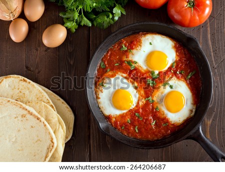 Shakshuka with eggs, tomato, and parsley in a cast iron pan.