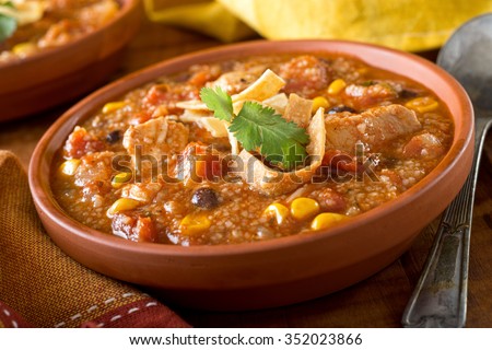 A bowl of delicious home made chicken tortilla soup with chicken, corn, black bean, tomato, homini, and tortilla.