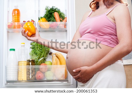 pregnant woman and refrigerator with health food vegetables and fruits