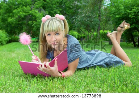 young blonde woman reading book in park on green grass