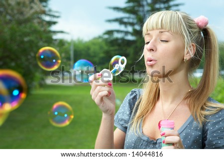 young girl makes soap bubble on grass