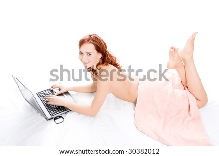spa naked red beautiful girl lays on white covered by a pink towel and works on laptop