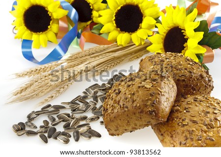 Three full-grain rolls, sunflower seeds, wheat ears and sunflowers with colored ribbons on a white background