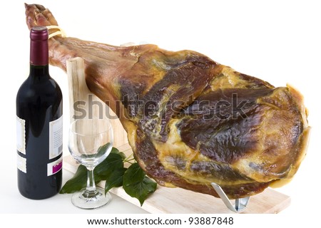 A front leg Serrano ham on displayed on a wooden rack and a bottle of red wine with a wine glass on a white background.