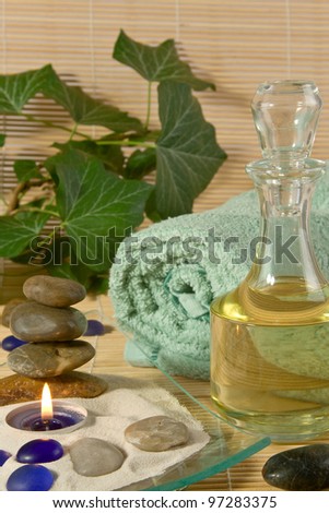 A bottle of massage oil, a burning scented candle, a bath towel and stones