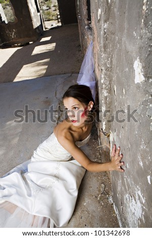 A beautiful thin bride with red makeup leans against a wall inside an old building