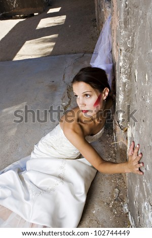 A beautiful thin bride with red makeup leans against a wall inside an old building