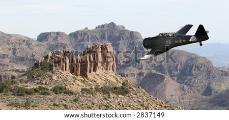 An old military prop plane flies low over a desert landscape in the superstition mountains of Arizona. Taken from on top of the flatiron.