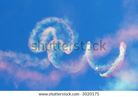 A parachute jumper with smoke canisters leaves a colorful trail in the blue sky