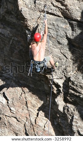 A rock climber works his way up a rock face protected by a rope clipped into bolts. He is wearing a helmet and quickdraws dangle from his harness. The route is in the desert southwest United States.