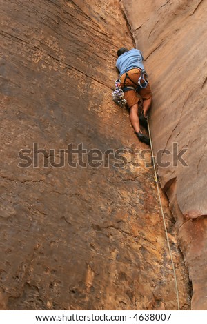 A powerful climber works his way up a crack in the cliff. He is trad climbing using cams and a rope