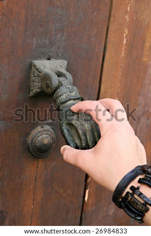 A female hand knocks an old-fashioned hand door knocker