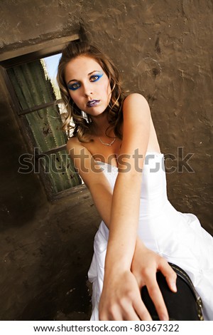 A beautiful bride in a flowing white gown with heavy eye makeup leans on a guitar case