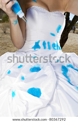 A bride with heavy makeup trashes her wedding gown using blue paint
