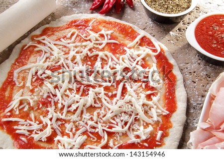 pizza preparation with cheese and tomato  surrounded by ingredients