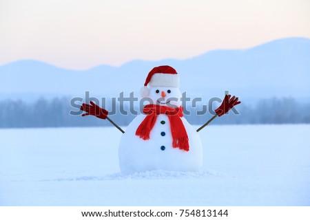 Snowman in red hat and scarf. Christmas scenery. High mountains at the background. Ground covered by snow. Nice cold winter day.