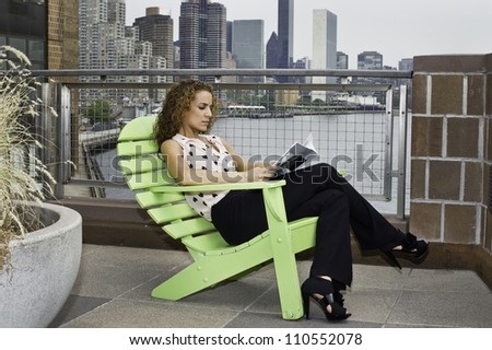A pretty woman is sitting on a chair outside, reading and relaxing. The background is high building skyline in a big city./Reading Outside