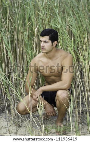 A young guy is squatting in a reed field and thinking/Thinking outdoor