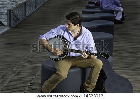 Looking around  and sitting on a fancy bench a young musician is playing a banjo/Play Music