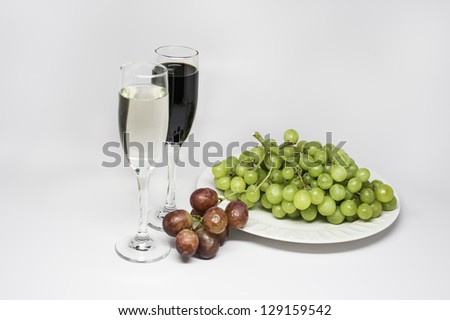 One plate of green grapes, a few of red grapes,  and one glass of white wine and one glass of red wine