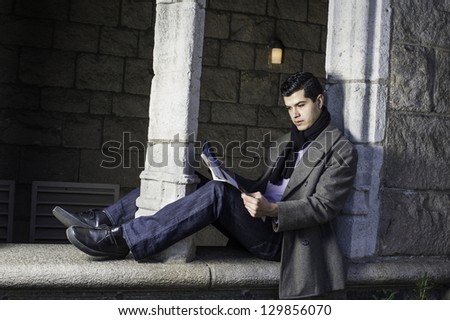 A young guy is sitting on a old window frame and reading/Reading