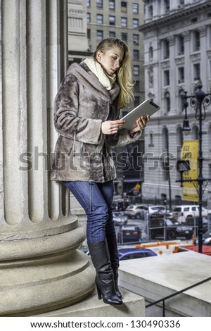 Dress heavily, a young blonde lady is standing up and studying outside./Study Outside