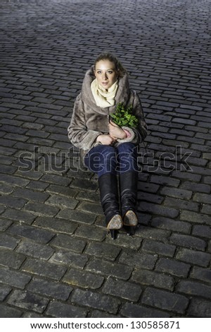 A girl holding a bunch of green plants is sitting on an old brick ground/Hope