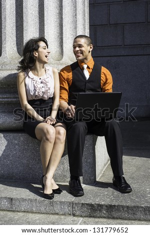 A young couple of businessman and businesswoman are working together outside, talking and laughing./Working Together