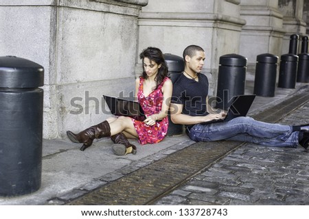 A guy and a girl are sitting separately on the street, busily working on their computers./Studying Outside