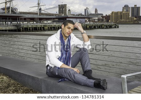 A young student is sitting by a river, scratching his head and into deeply thinking./Sitting Down and Thinking