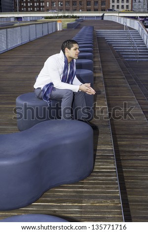 A young guy is sitting on a modern style bench and waiting for you.