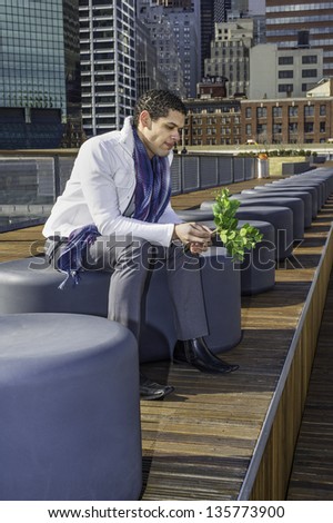 Holding a bunch of green leaves, a young guy is sitting on a modern style bench and thinking.